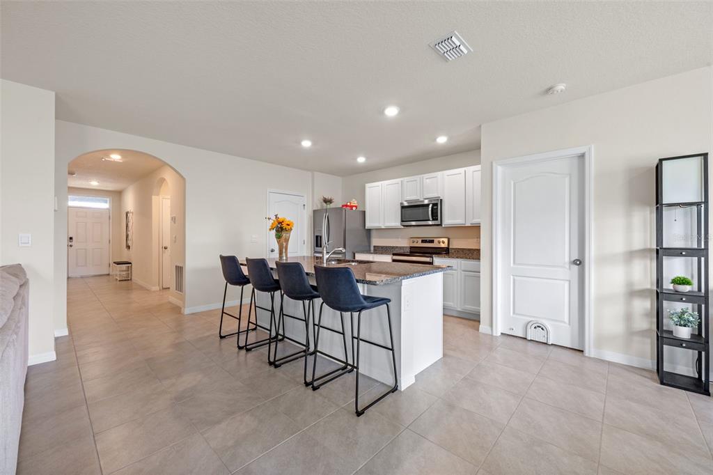 A kitchen with a granite-topped island, dark bar stools, and white cabinets — 5362 DOUGLAS FIR DRIVE, ST CLOUD, FL