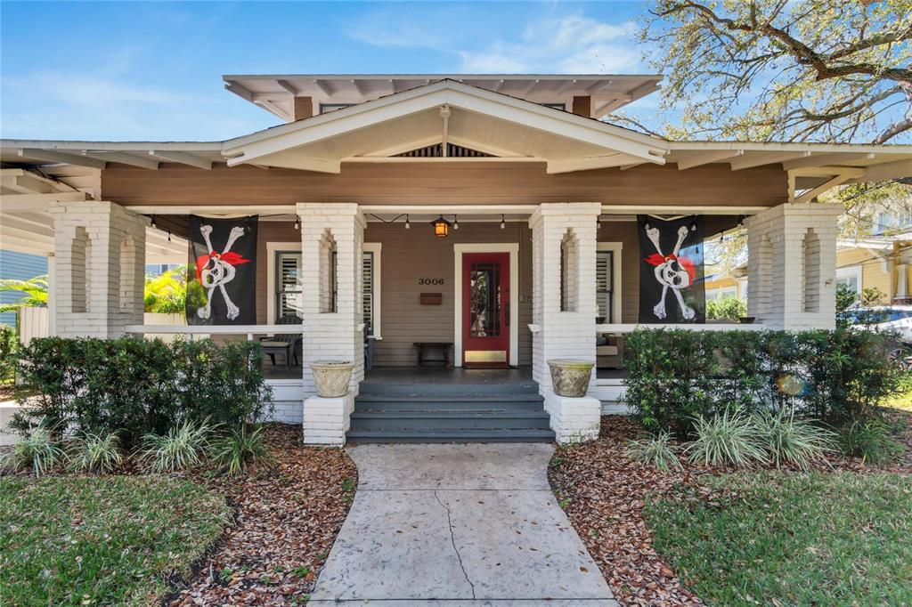 A single-story bungalow with a covered front porch, white brick pillars, and two pirate flags — 3006 W HARBOR VIEW AVENUE, TAMPA, FL