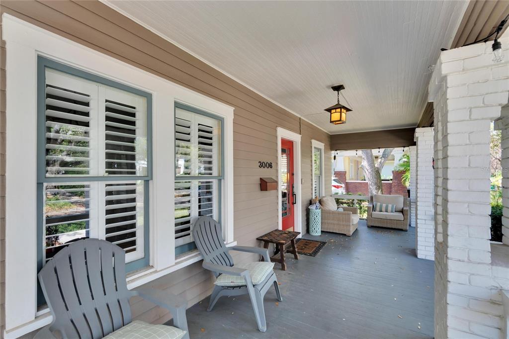 A covered front porch features gray wooden chairs, a red door, and white brick columns — 3006 W HARBOR VIEW AVENUE, TAMPA, FL