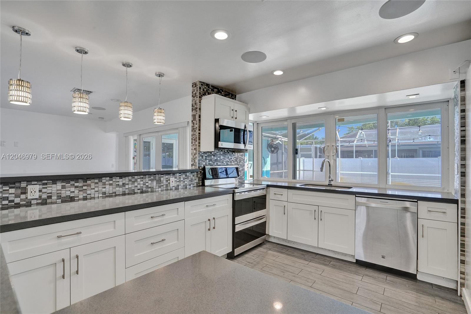 A modern kitchen features white cabinetry, dark countertops, a mosaic backsplash, and stainless steel appliances — 9240 54th St, Cooper City FL 33328, COOPER CITY, FL