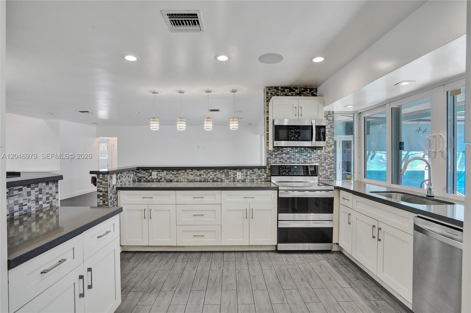 A modern kitchen features white cabinets, dark countertops, a mosaic backsplash, and gray wood-look flooring — 9240 54th St, Cooper City FL 33328, COOPER CITY, FL