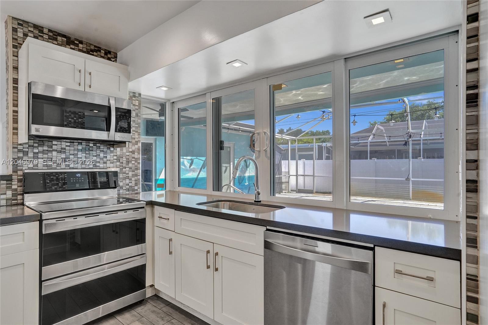 A kitchen features white cabinets, stainless steel appliances, dark countertops, and a large window view — 9240 54th St, Cooper City FL 33328, COOPER CITY, FL