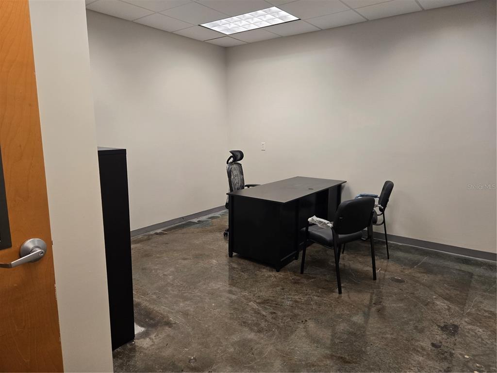 A small office features a black desk, three chairs, and a stained concrete floor — 14202 N NEBRASKA AVENUE UNIT 14202, TAMPA, FL