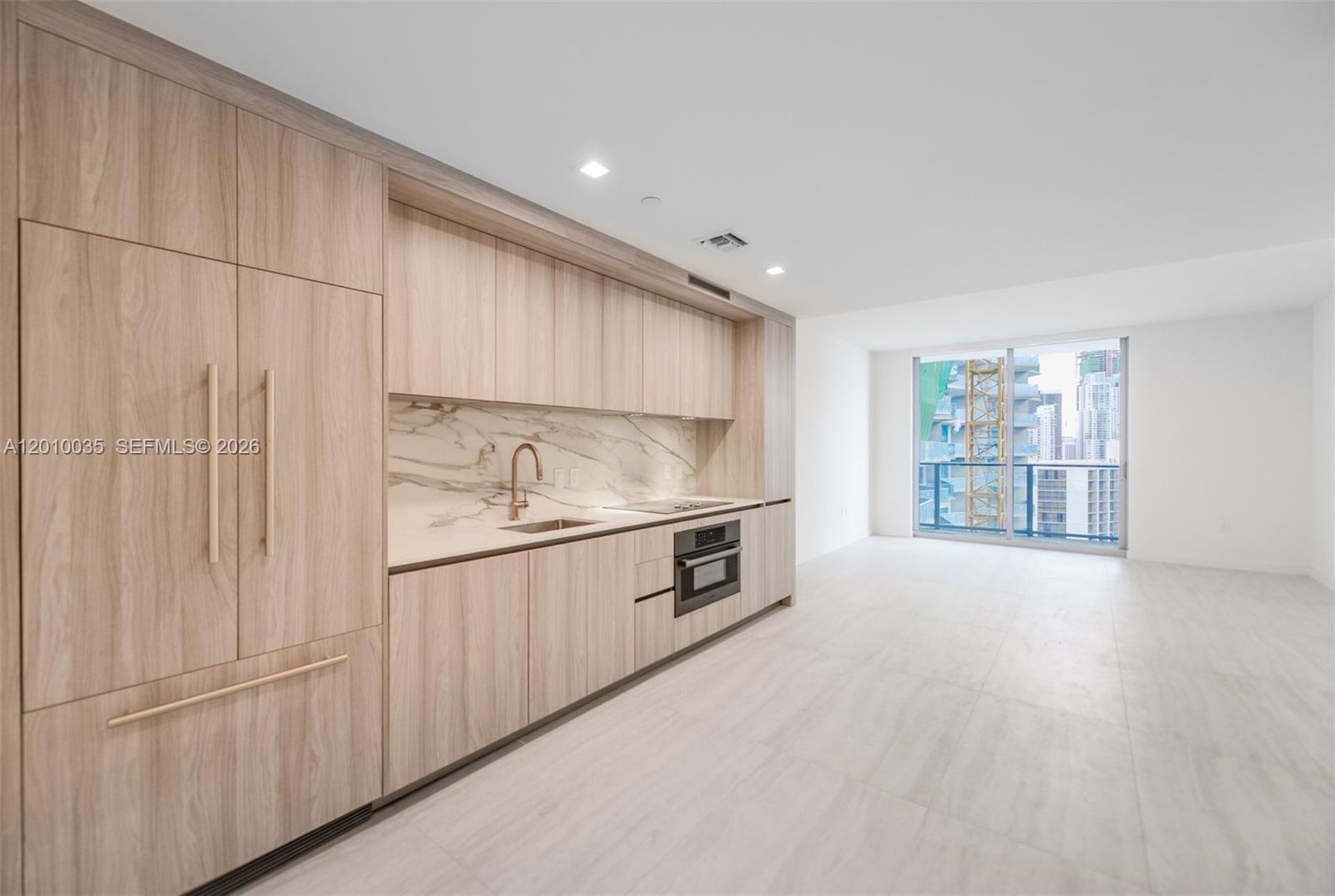 A modern kitchen features light wood cabinetry, marble backsplash, and stainless steel appliances — 77 SE 5 Street # 2603, Miami FL 33131, MIAMI, FL