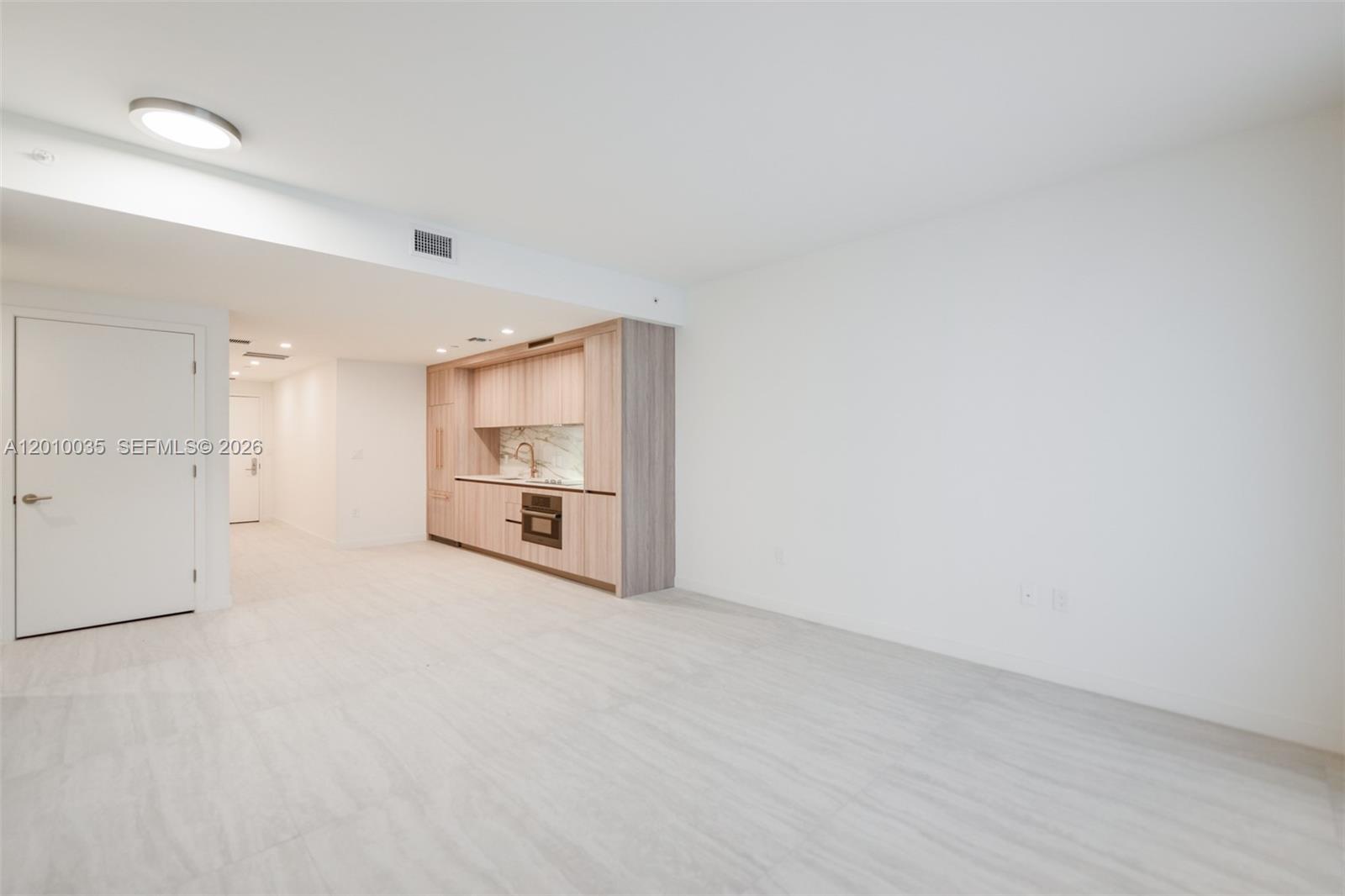 A minimalist studio apartment features light wood cabinetry, white walls, and light-colored tile flooring — 77 SE 5 Street # 2603, Miami FL 33131, MIAMI, FL