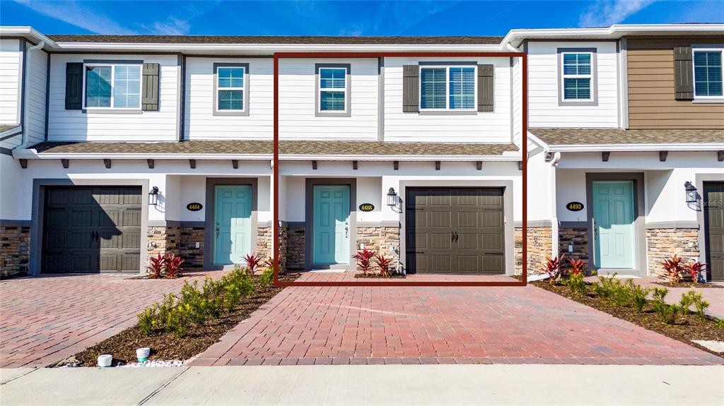 The exterior of a two-story townhouse features a stone base, white siding, and a garage — 4488 CAMPSITE LOOP, ORLANDO, FL