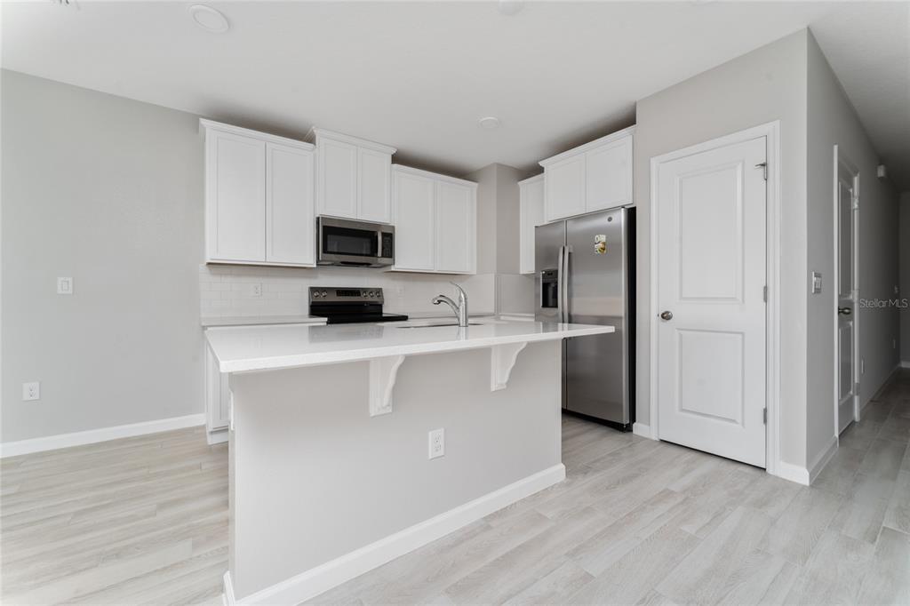 A kitchen with white cabinets, stainless steel appliances, a center island, and light wood flooring — 4488 CAMPSITE LOOP, ORLANDO, FL