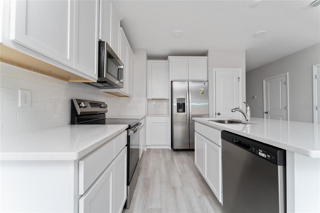 A modern kitchen features white cabinets, stainless steel appliances, and a white quartz island — 4488 CAMPSITE LOOP, ORLANDO, FL