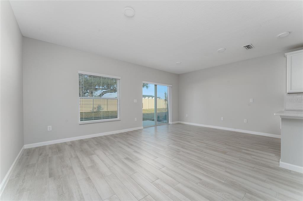 An empty living room features light gray walls, wood-look flooring, a sliding glass door, and windows — 4488 CAMPSITE LOOP, ORLANDO, FL
