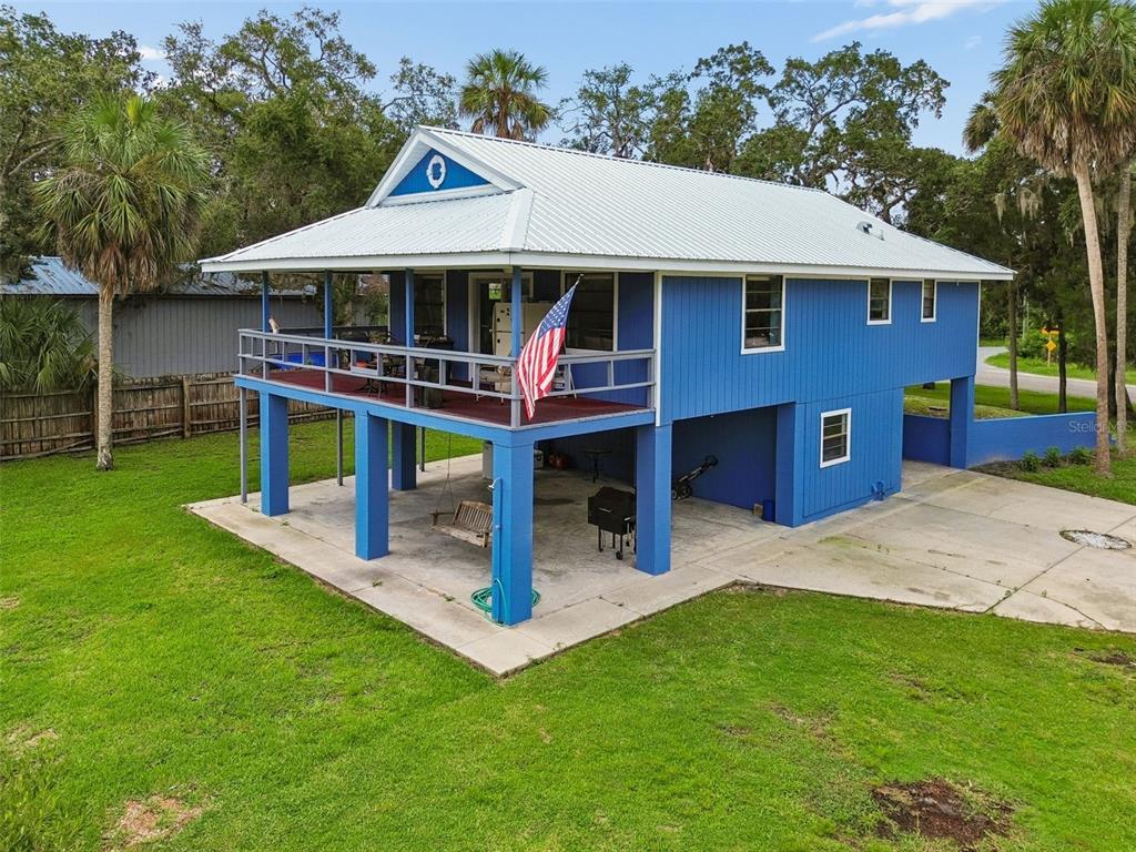 An elevated blue house with a metal roof sits on a grassy lot beside a canal — 1455 S OZELLO TRAIL, CRYSTAL RIVER, FL
