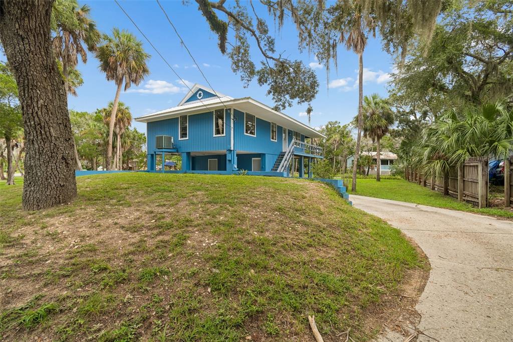 An elevated blue house with a metal roof sits on a grassy lot near water — 1455 S OZELLO TRAIL, CRYSTAL RIVER, FL