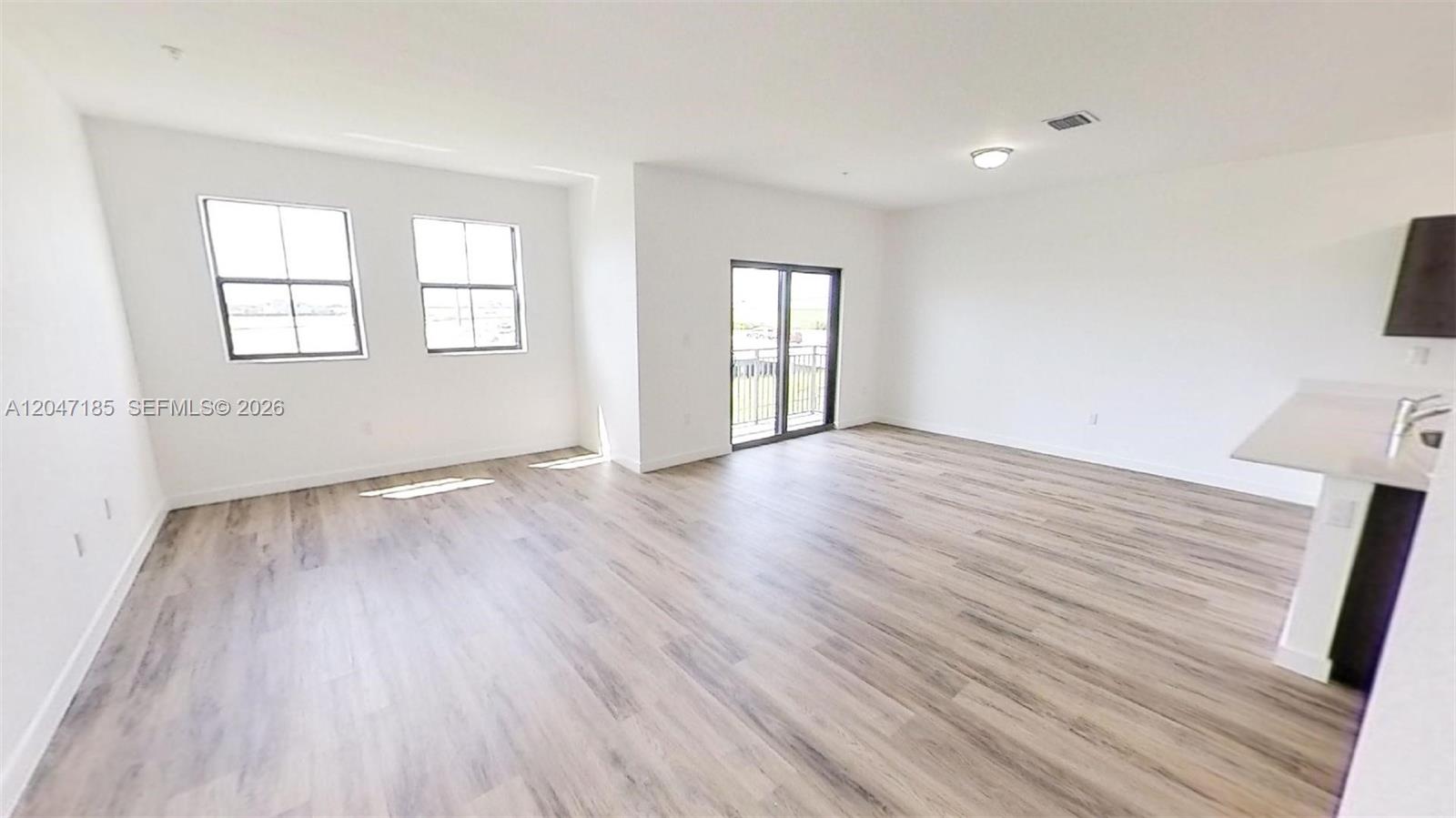 An open-concept living area features light wood-look flooring, white walls, and a sliding glass door — 15650 SW 136th St # 207, Miami FL 33196, MIAMI, FL