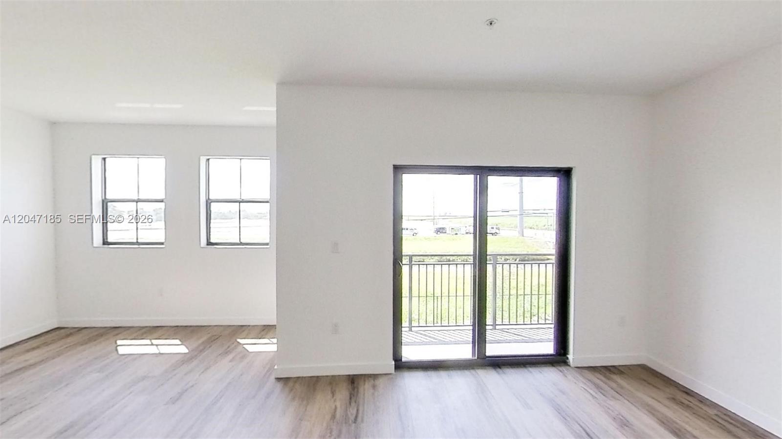 This room features light wood-look flooring, white walls, two windows, and a sliding glass door — 15650 SW 136th St # 207, Miami FL 33196, MIAMI, FL