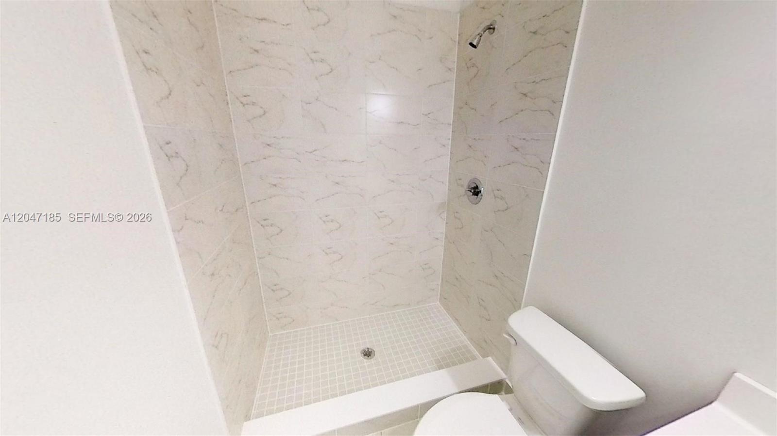 A walk-in shower with marble-patterned tile walls sits next to a white toilet — 15650 SW 136th St # 207, Miami FL 33196, MIAMI, FL