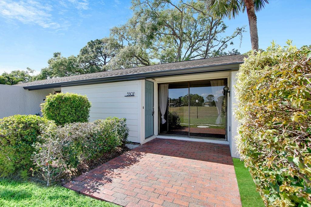 A brick walkway leads to the front entrance of a house with white siding — 3507 LONGMEADOW UNIT 4, SARASOTA, FL