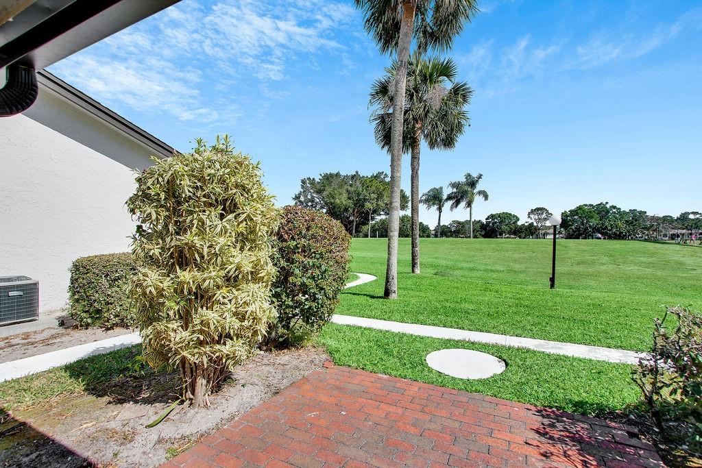 A brick patio overlooks a grassy lawn with palm trees and a clear blue sky — 3507 LONGMEADOW UNIT 4, SARASOTA, FL