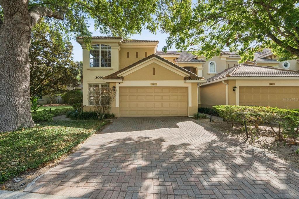 A two-story townhouse with a tan stucco exterior, a brick paver driveway, and a garage — 3099 METRO SEVILLA DRIVE UNIT 101, ORLANDO, FL
