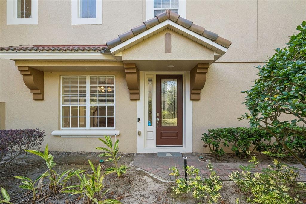 The exterior of a tan stucco home features a brown front door and a window — 3099 METRO SEVILLA DRIVE UNIT 101, ORLANDO, FL