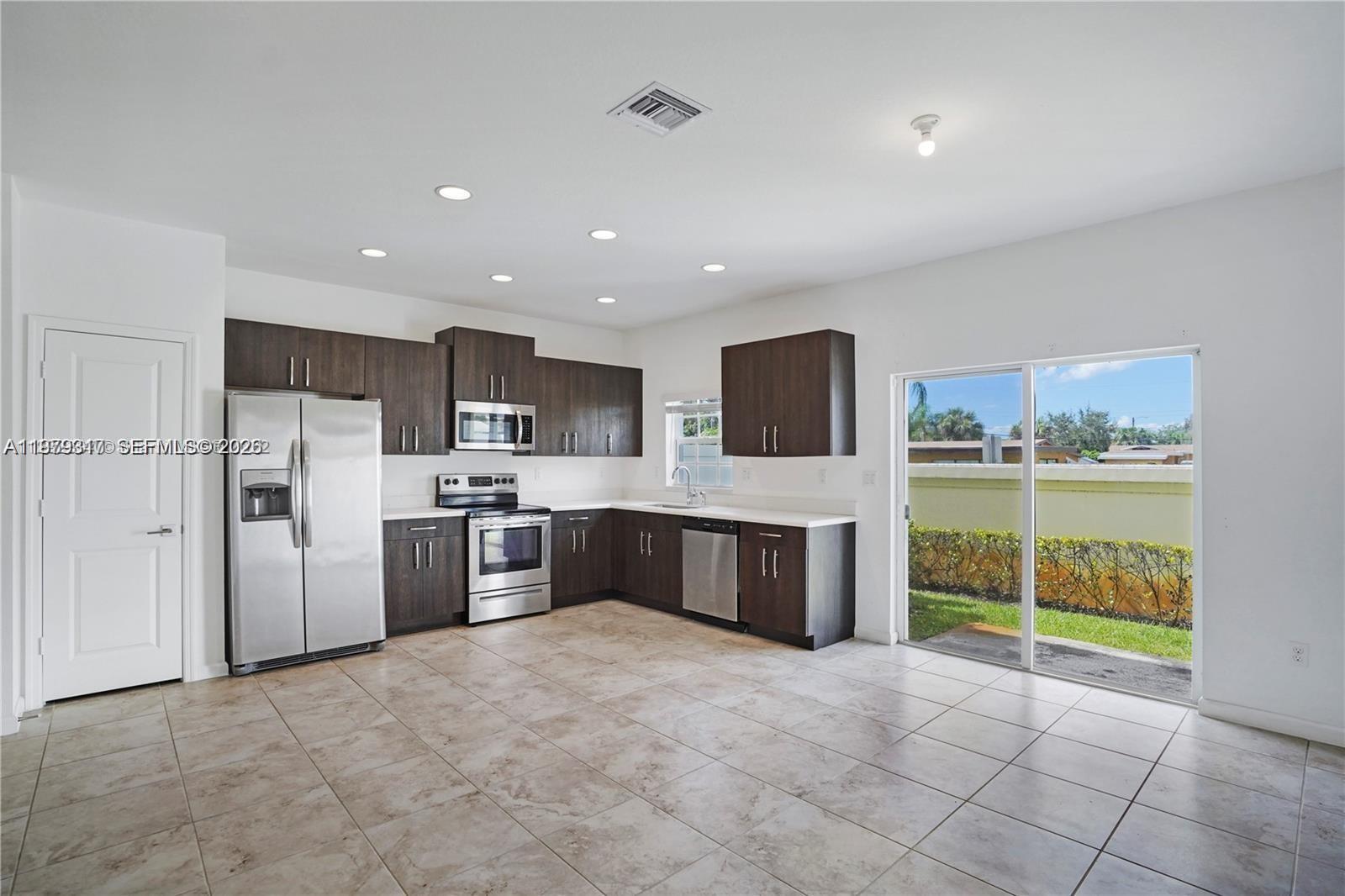 A kitchen features dark wood cabinets, stainless steel appliances, and tile flooring with sliding glass doors — 1121 NW 41st Ln, Lauderhill FL 33313, LAUDERHILL, FL
