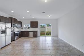 A kitchen with dark wood cabinets and stainless steel appliances opens to a tiled living area — 1121 NW 41st Ln, Lauderhill FL 33313, LAUDERHILL, FL