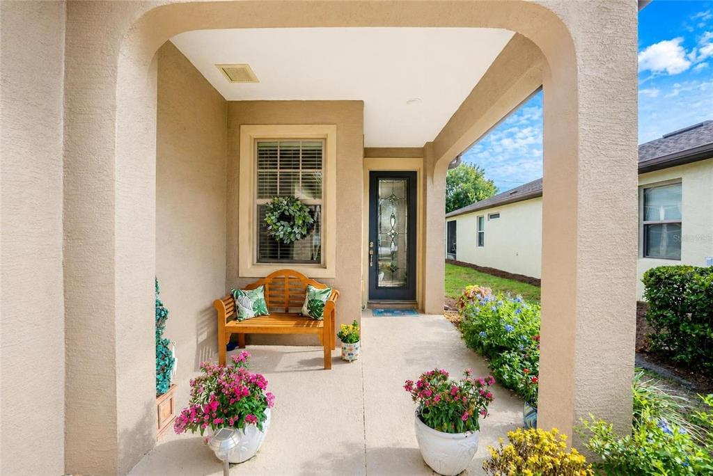 A covered front porch features a wooden bench, potted flowers, and a glass-paneled front door — 7676 SW 94TH CIRCLE, OCALA, FL