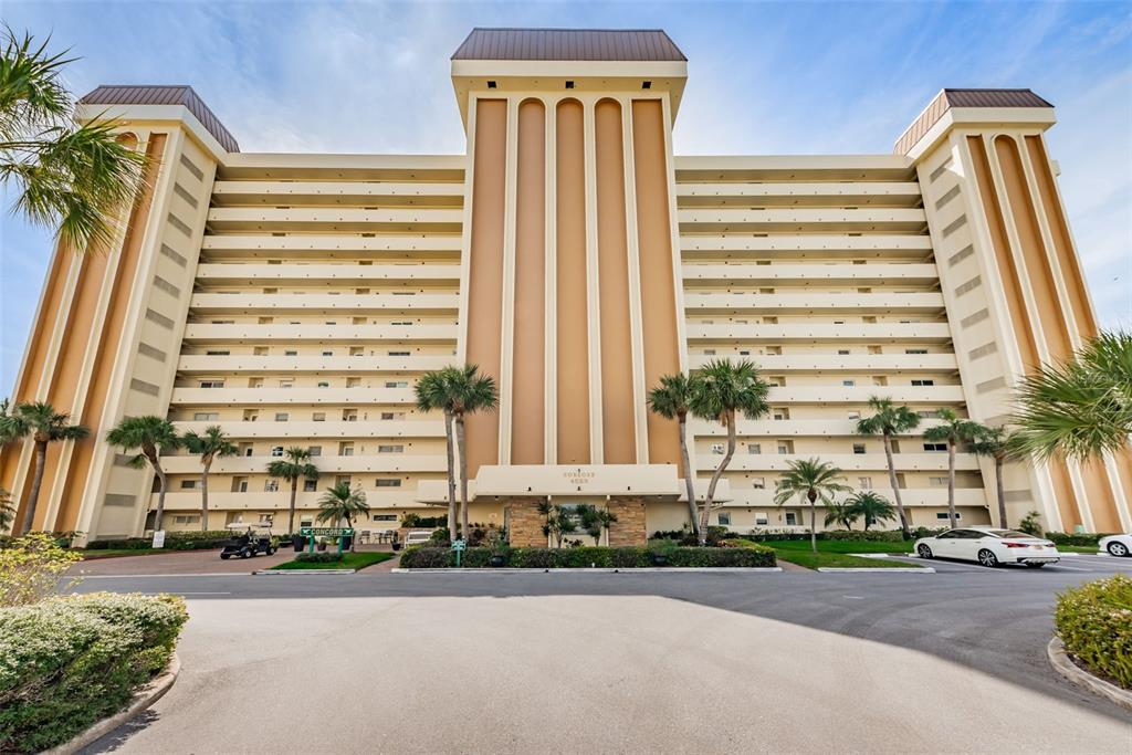 A multi-story residential building with a tan facade, balconies, and palm trees in the foreground — 4525 COVE CIRCLE UNIT 604, ST PETERSBURG, FL