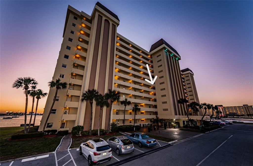 A multi-story residential building exterior at sunset with a white arrow pointing to a balcony — 4525 COVE CIRCLE UNIT 604, ST PETERSBURG, FL