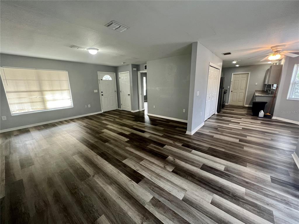 An open-concept living area features gray walls, wood-look plank flooring, and a kitchen in the background — 45 PINE CIRCLE, OCALA, FL