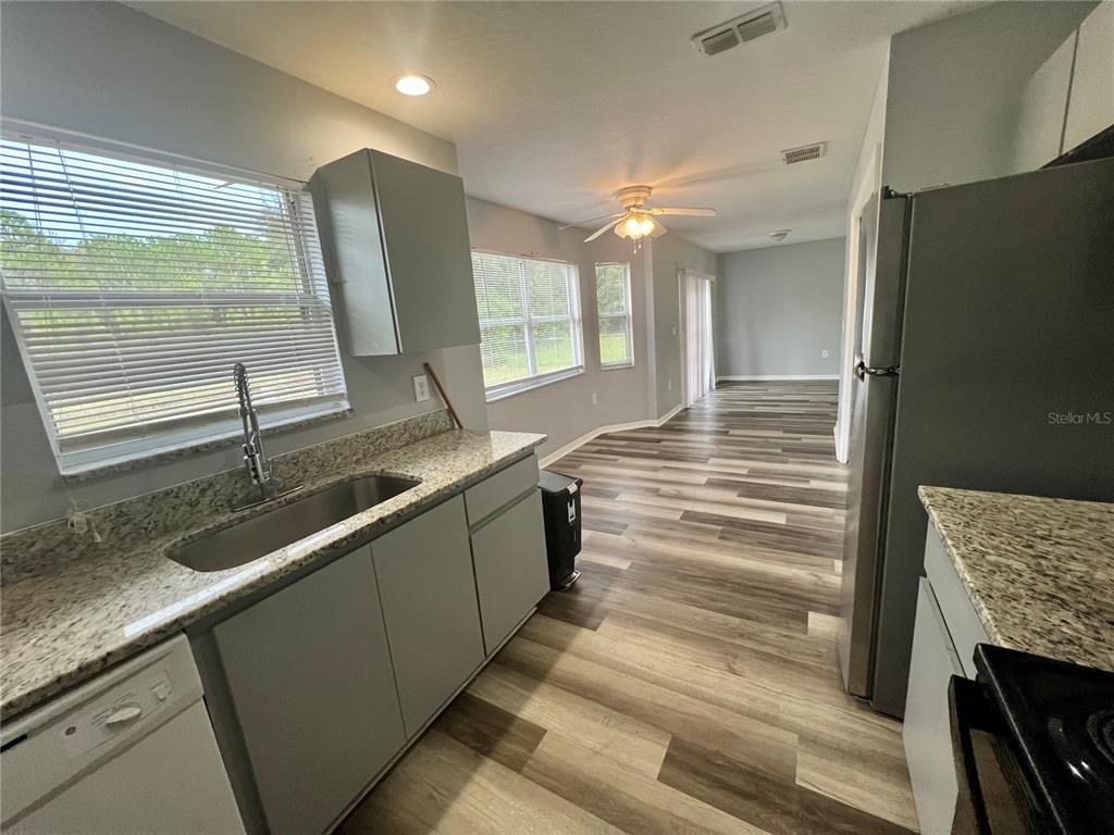 A kitchen with gray cabinets, granite countertops, and wood-look flooring leads into an open living area — 45 PINE CIRCLE, OCALA, FL