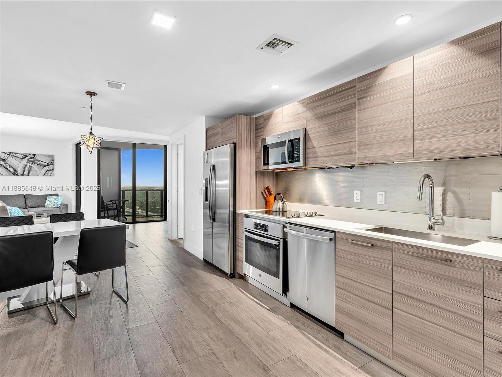 A modern kitchen features wood-grain cabinets, stainless steel appliances, and an adjacent dining area — 121 NE 34th St # 3114, Miami FL 33137, MIAMI, FL