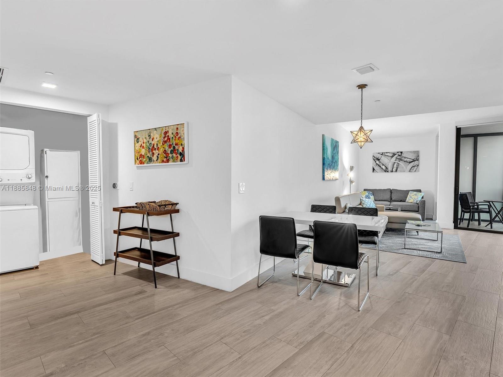 A modern open-concept living and dining area features white walls, wood-look flooring, and a laundry closet — 121 NE 34th St # 3114, Miami FL 33137, MIAMI, FL