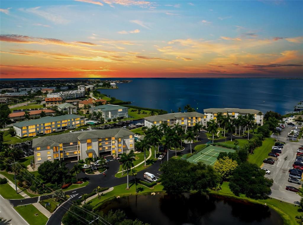 An aerial view of a waterfront apartment complex with a tennis court and parking lot — 1250 W MARION AVENUE UNIT 242, PUNTA GORDA, FL