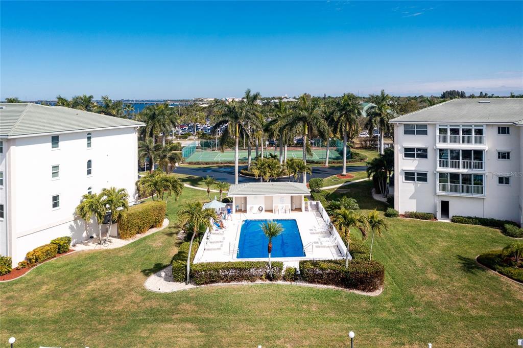 An aerial view shows a swimming pool and tennis courts between two residential apartment buildings — 1250 W MARION AVENUE UNIT 242, PUNTA GORDA, FL
