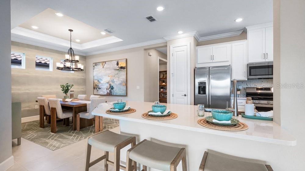 A kitchen with white cabinets and a stainless steel refrigerator overlooks a dining area — 3864 IMMACOLATA WAY, WESLEY CHAPEL, FL