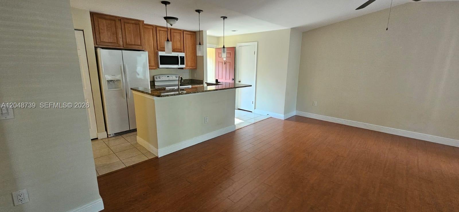 An open-concept kitchen with wood cabinets and a breakfast bar overlooks a living area — WEST PALM BEACH, FL