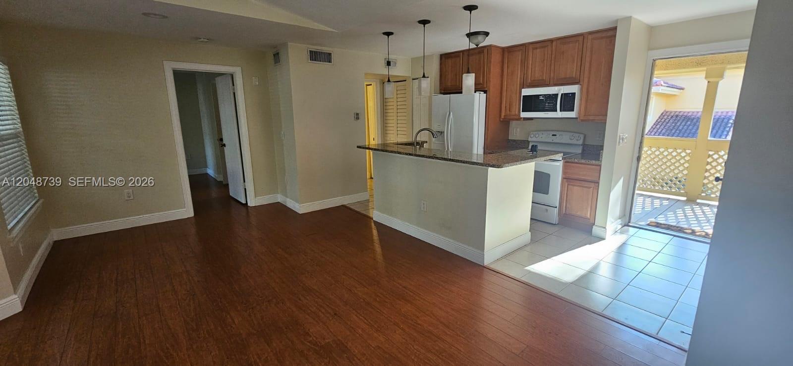 An open-concept kitchen with wood cabinets and a breakfast bar overlooks a hardwood living area — WEST PALM BEACH, FL