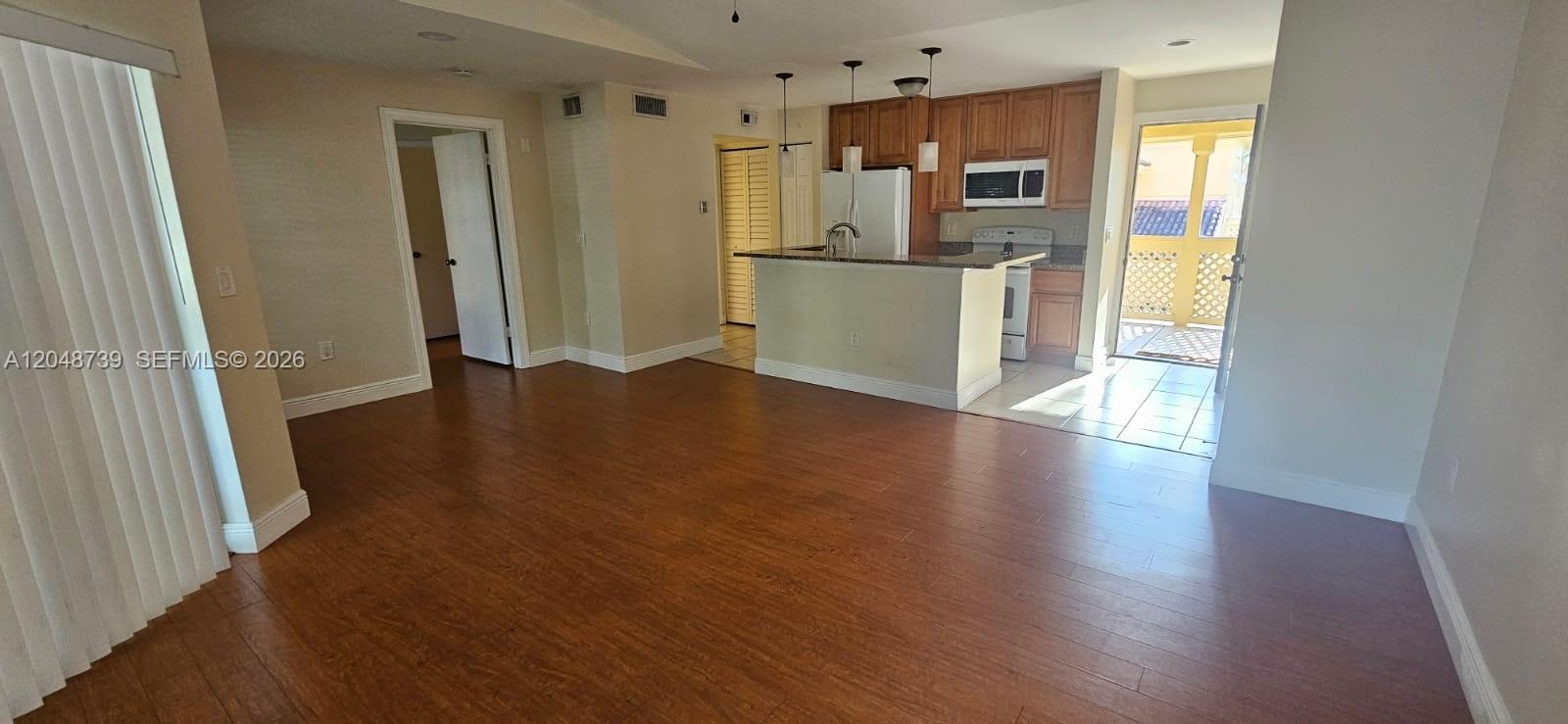 An open-concept living area features wood-look flooring, a kitchen with wood cabinets, and a balcony — WEST PALM BEACH, FL