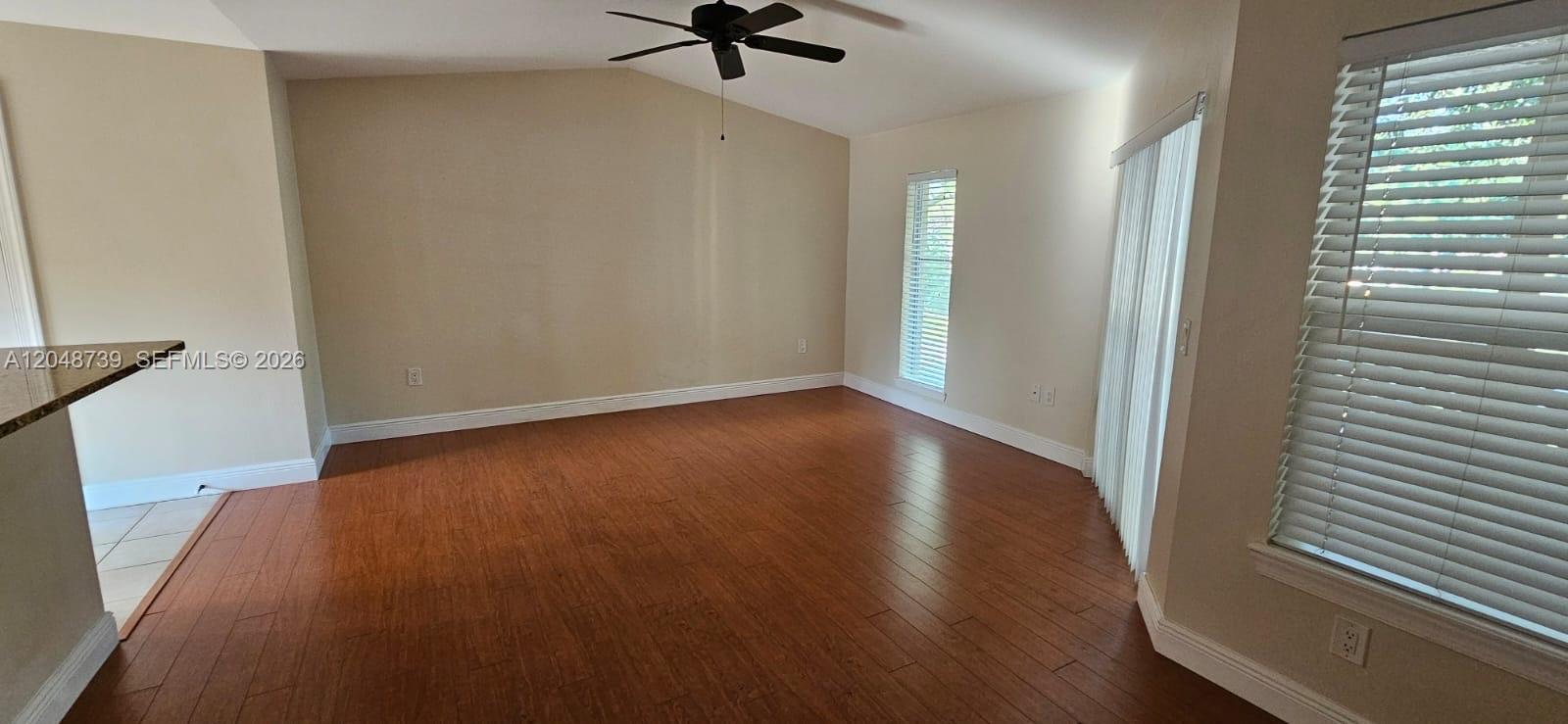 This living room features wood-look flooring, beige walls, a ceiling fan, and large windows — WEST PALM BEACH, FL
