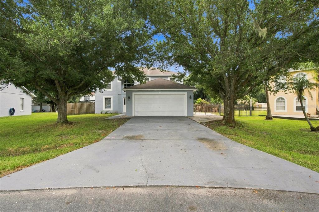 A two-story house with a front-facing garage and a concrete driveway framed by large trees — 621 JUILLAC WAY, KISSIMMEE, FL