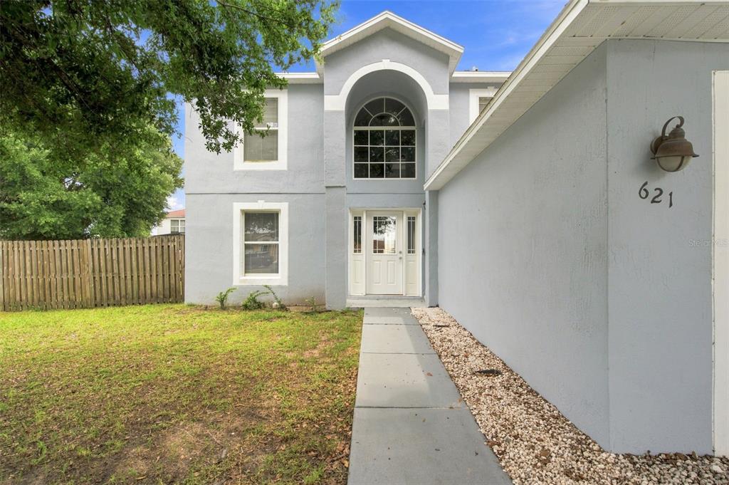 A two-story house with light blue stucco siding, a white front door, and a concrete walkway — 621 JUILLAC WAY, KISSIMMEE, FL