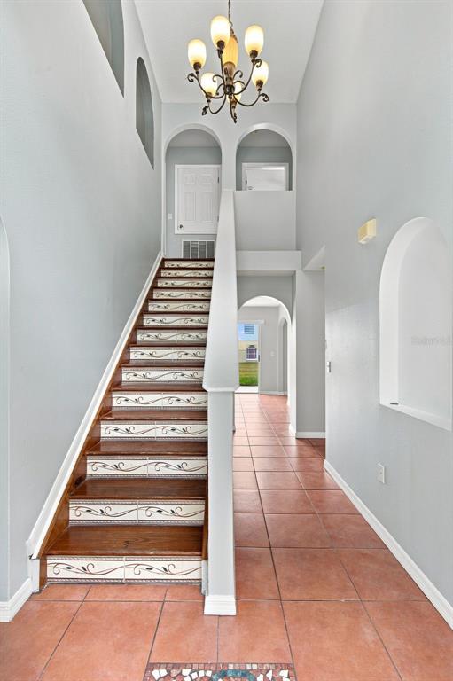 An entryway features a staircase with decorative tile risers, terracotta floor tiles, and a chandelier — 621 JUILLAC WAY, KISSIMMEE, FL