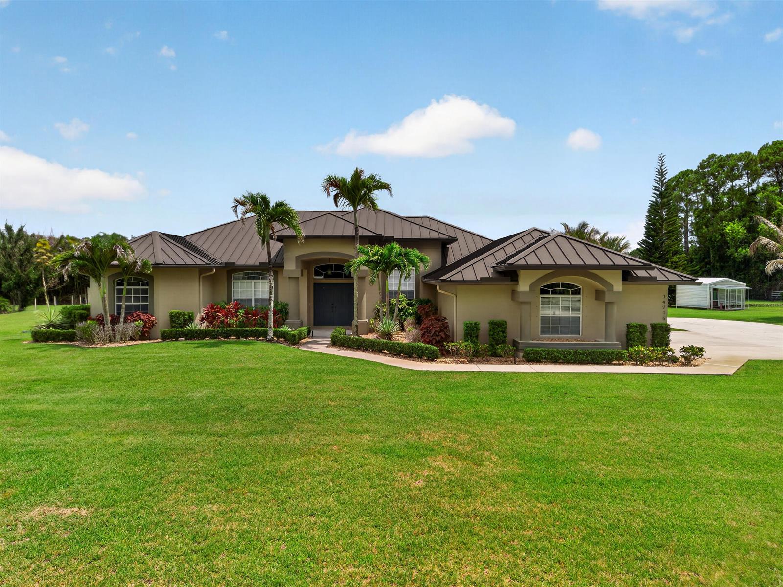 A single-story house with a dark metal roof, tan stucco walls, and palm trees — 14716 83rd Lane N, Loxahatchee FL 33470, LOXAHATCHEE, FL