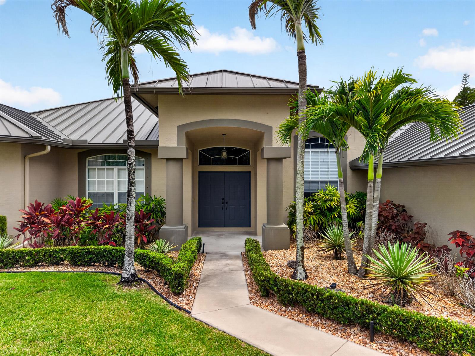 A single-story house with a metal roof, dark double front doors, and palm tree landscaping — 14716 83rd Lane N, Loxahatchee FL 33470, LOXAHATCHEE, FL