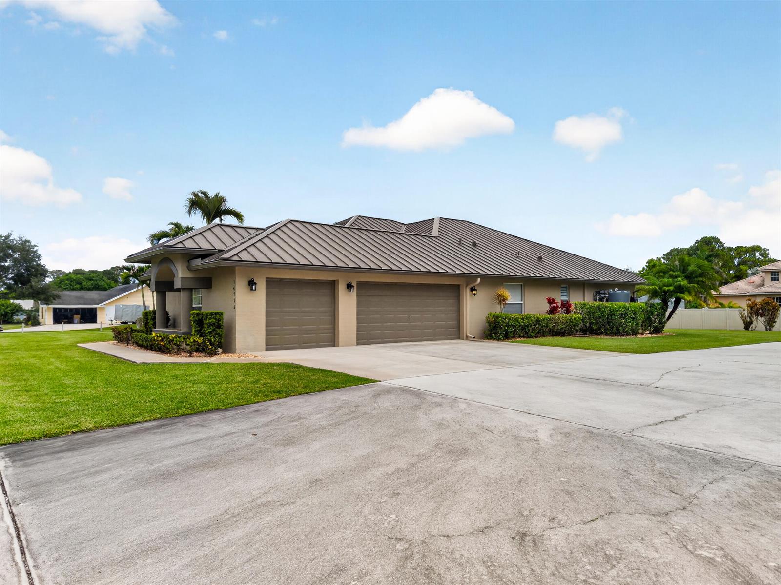 A tan house with a metal roof and a three-car garage sits on a lawn — 14716 83rd Lane N, Loxahatchee FL 33470, LOXAHATCHEE, FL