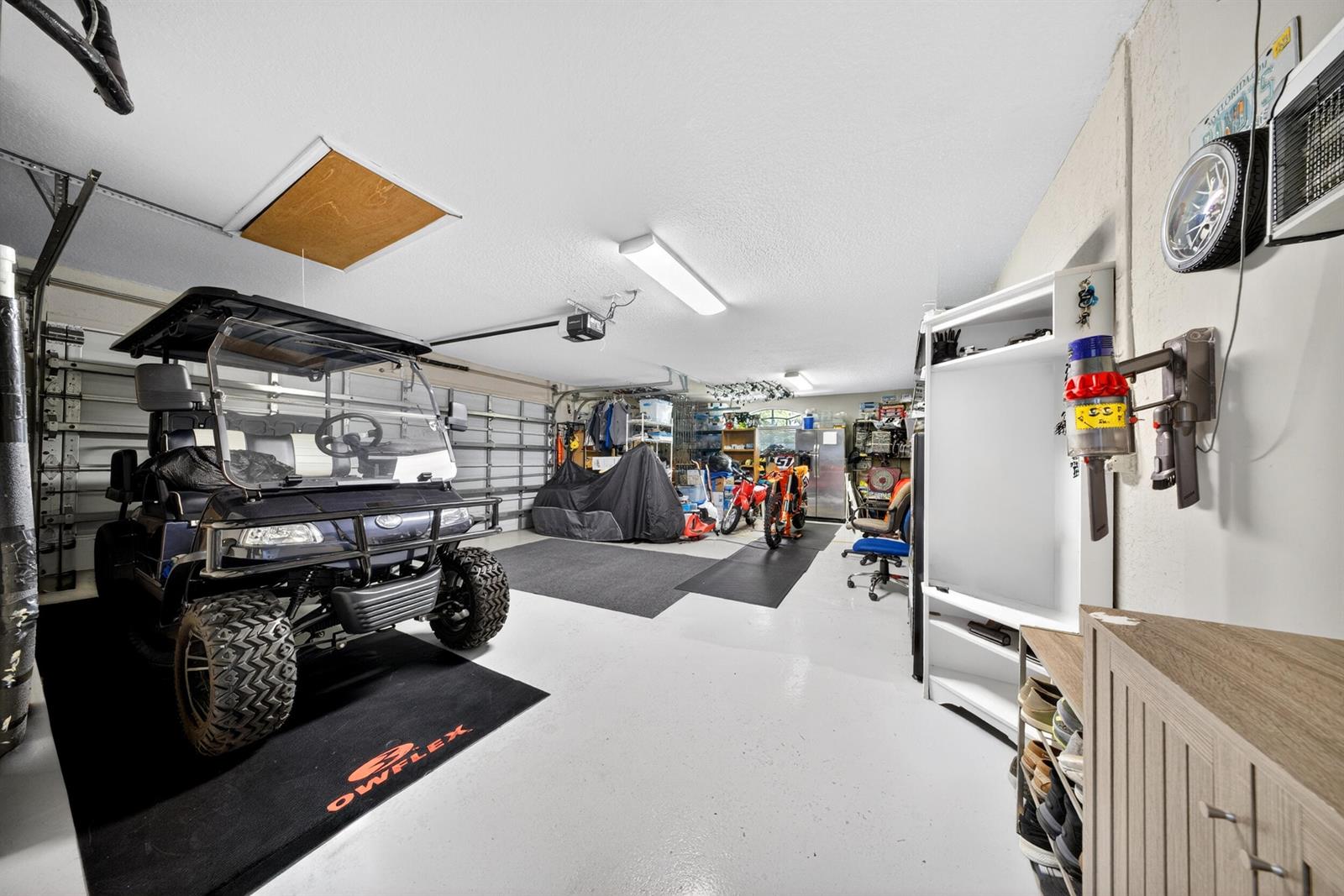 A garage features a golf cart, motorcycles, storage shelving, and a white epoxy floor — 14716 83rd Lane N, Loxahatchee FL 33470, LOXAHATCHEE, FL