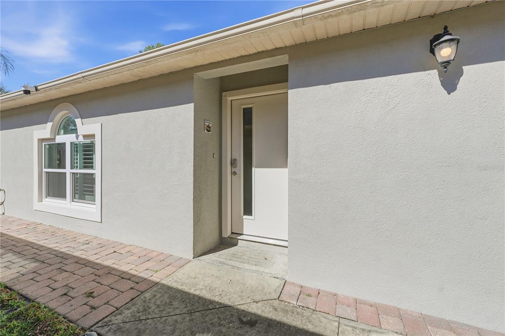 A beige exterior wall features a white front door, a window with shutters, and a light — 139 PLACID WOODS COURT, SANFORD, FL