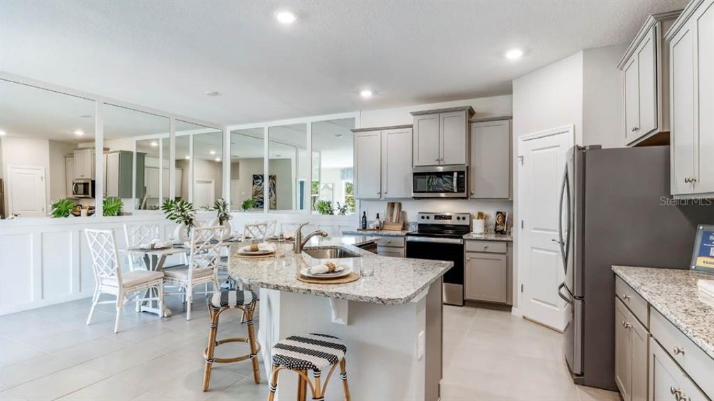 A kitchen with gray cabinets, granite countertops, and an island with two stools — 6245 PARMERON LANE, SARASOTA, FL