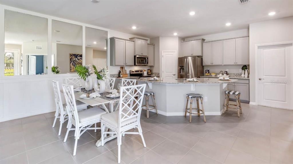A kitchen and dining area with light gray cabinets, granite countertops, and white lattice chairs — 6245 PARMERON LANE, SARASOTA, FL