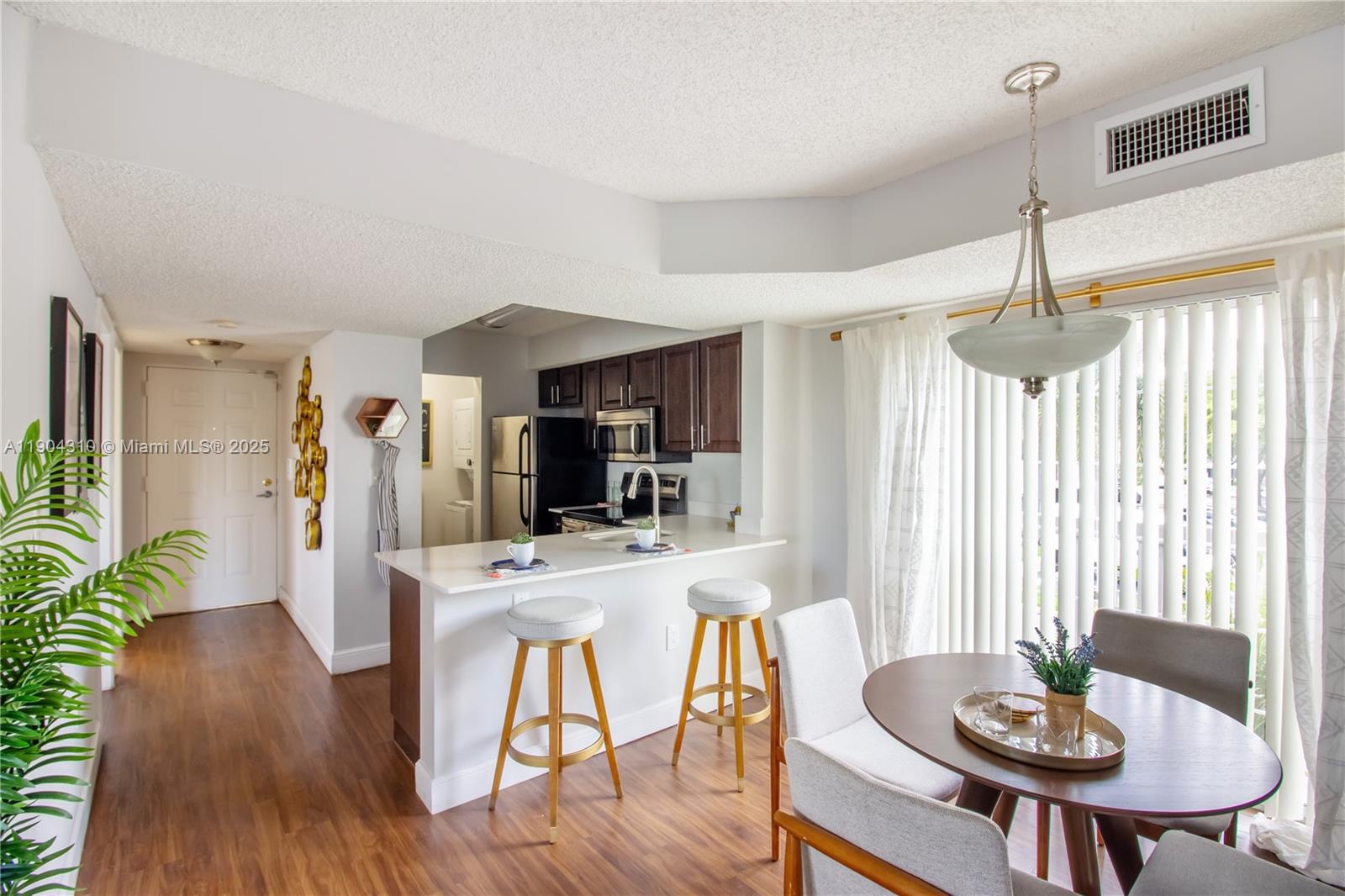 A kitchen with dark cabinets and a breakfast bar overlooks a dining area with seating — 17230 NW 64th Ave, Miami Lakes FL 33015, MIAMI LAKES, FL