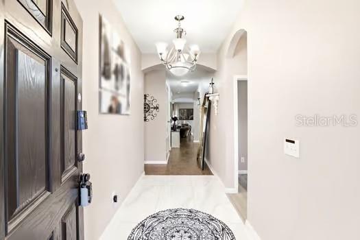 A bright entryway features a dark wood door, white tile floors, and a crystal chandelier — 2825 RUNNING BROOK CIRCLE, KISSIMMEE, FL